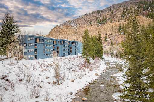 A blue building is situated by a stream in a snowy landscape.