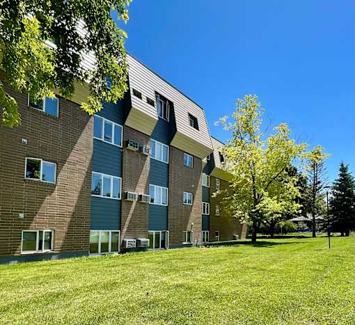 a brick apartment building with green grass and trees