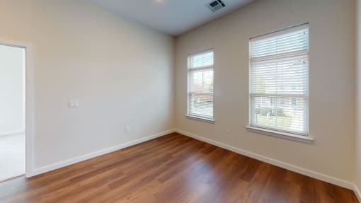 an empty living room with wood floors and two windows
