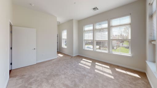 an empty living room with large windows and carpeting