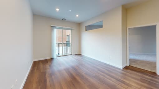 an empty living room with wood flooring and a door to a balcony