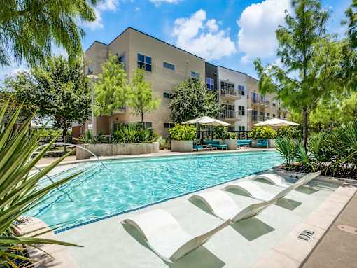 A swimming pool with sun loungers and a building in the background.at Infinity on Yorktown, Texas
