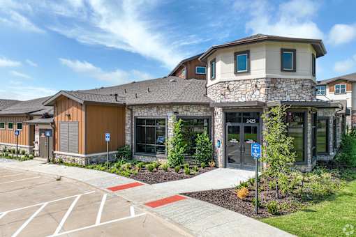 a building with stone and wood exterior and a sidewalk in front of it at Creekside at Grand Prairie, Grand Prairie, TX