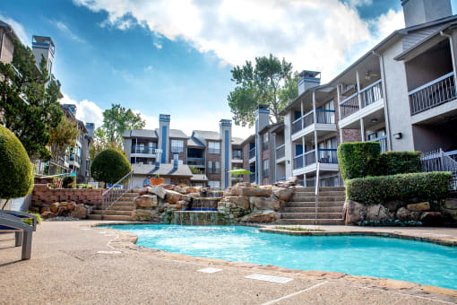 a swimming pool with a waterfall in front of an apartment building at Infinity on the Mark, Dallas, TX, 75243