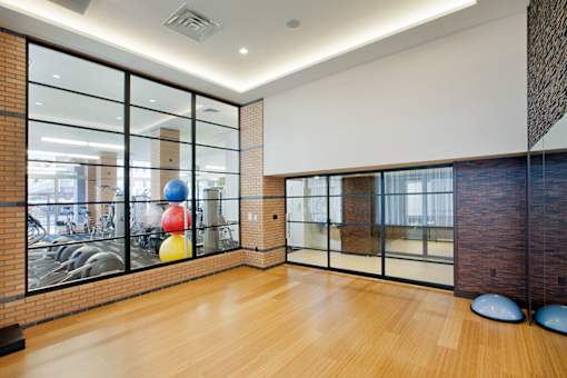 A room with a wooden floor and a glass wall with a view of a gym.