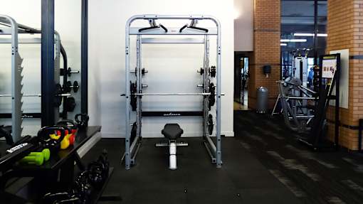 A gym with a squat rack, weight bench, and dumbbells.