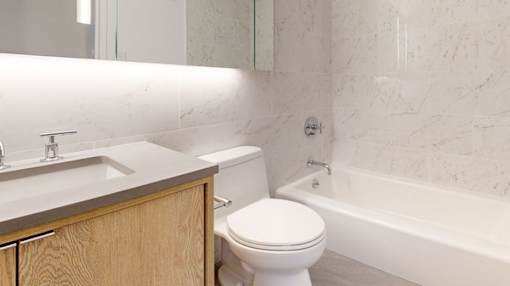 A white toilet sits next to a sink in a bathroom. at The Ellington Apartments, Apartments, New York, NY