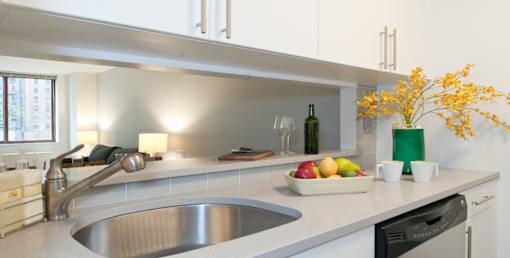 A modern kitchen with a stainless steel sink and a green vase with yellow flowers. at The Ellington Apartments, New York, New York