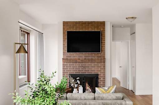 A living room with a fireplace and a flat screen TV mounted above it. at The Ellington Apartments, Apartments, New York, NY