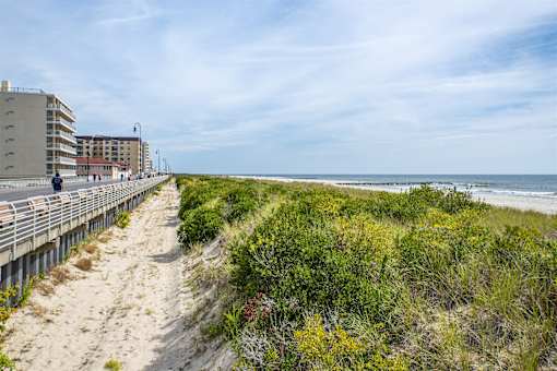 A beach scene with a boardwalk, people walking, and a building in the background.