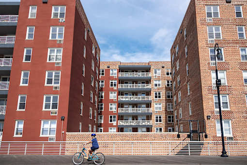 A person riding a bicycle in front of red brick buildings.