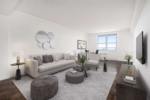 A modern living room with a grey sofa, a grey ottoman, a grey rug, a wooden coffee table, a flat screen TV, and a window with a view of the balcony.