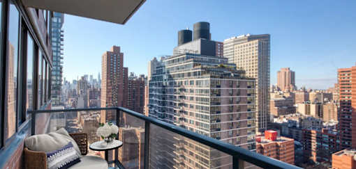 A balcony with a table and chairs overlooks a cityscape.at 301E94, New York, NY 10128 