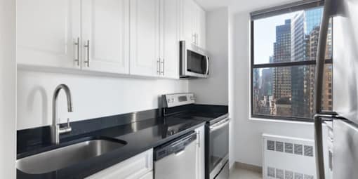 A modern kitchen with black countertops and white cabinets.at Carnegie Mews, New York, 10019