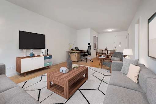 A living room with a grey couch, a wooden coffee table, and a television on the wall at The Caldwell Apartments, New York