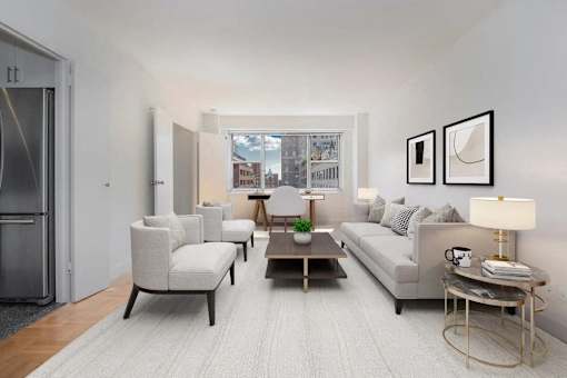 A modern living room with a grey sofa, a coffee table, and a large window at The Caldwell Apartments, New York, New York