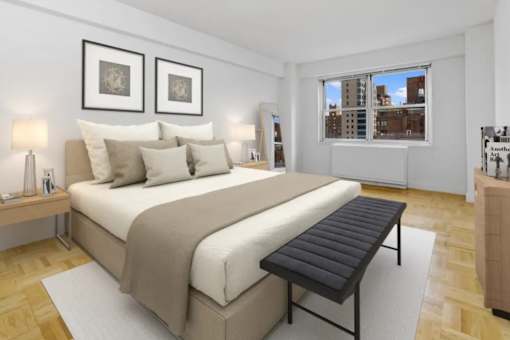 A bedroom with a large bed and a window overlooking a cityscape at The Caldwell Apartments, New York, NY
