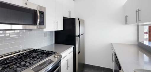 A black refrigerator sits in a kitchen with white cabinets at The Ellington Apartments, New York, 10019
