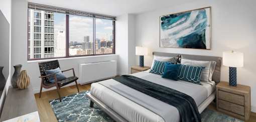 A bedroom with a large bed, a chair, and a painting on the wall at The Ellington Apartments, New York, NY, 10019