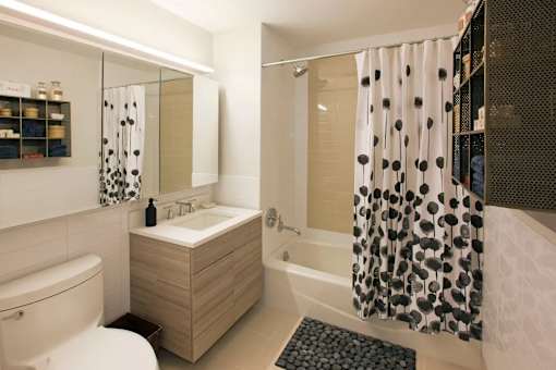A modern bathroom with a wooden vanity and a shower curtain with black and white polka dots at The Maximilian Apartments, Long Island City, NY