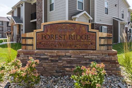 A sign that says Forest Ridge Villas in front of some houses.