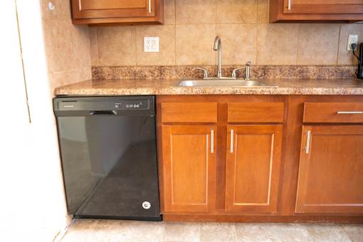 A black dishwasher is in a kitchen with wooden cabinets.