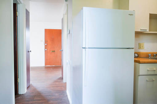 A white fridge in a kitchen with a wooden floor.