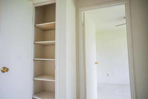 A white door with a gold handle is open to a white hallway.