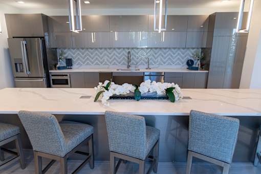 A modern kitchen with a marble countertop and grey chairs.