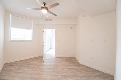 A room with a ceiling fan and a door leading to another room.