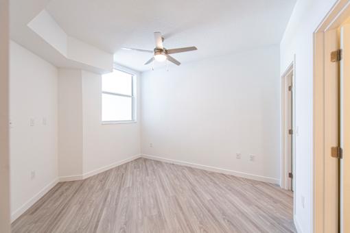 A room with a ceiling fan and light, hardwood floors, and a window.