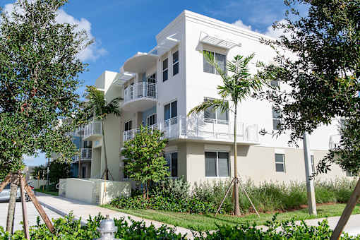 A white apartment building with balconies and trees in front.