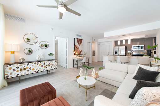 A living room with a white couch, a brown ottoman, and a ceiling fan.