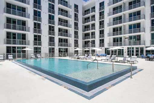 A large swimming pool in front of a building with white balconies.