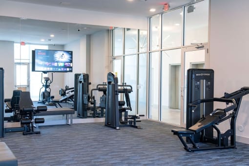 a gym with cardio equipment and a tv in a room with glass walls