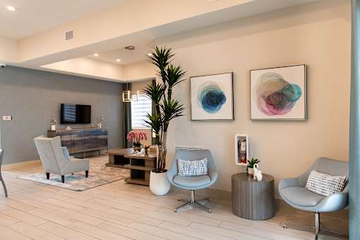A living room with a grey sofa, a grey armchair, a wooden coffee table, a potted plant, and two framed artworks on the wall.