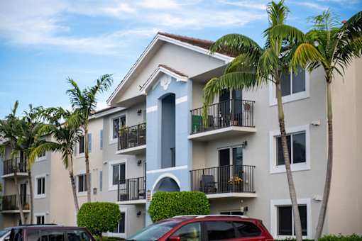A row of apartment buildings with balconies and palm trees in front.
