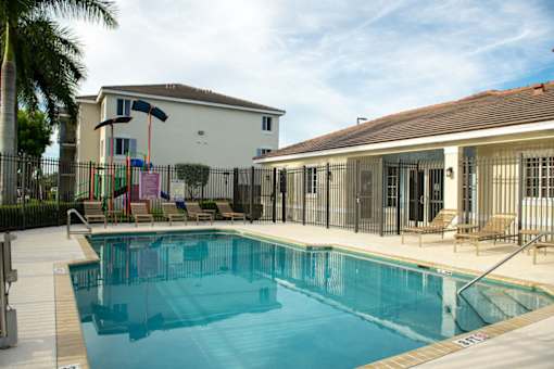 A swimming pool in front of a house with a playground.
