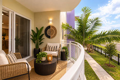 A balcony with a wicker chair and a table with a plant on it.