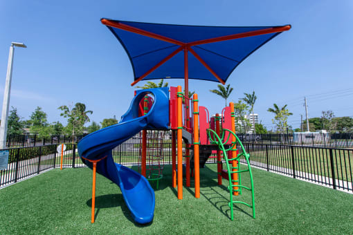 a playground with a swing set and a blue umbrella