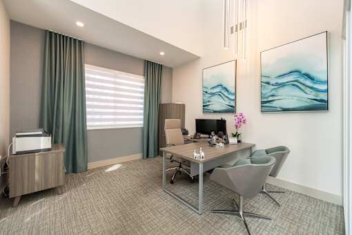 A modern office room with a desk, chairs, and two paintings on the wall.