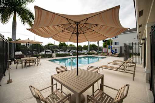 A large umbrella shades a table and chairs by a pool.