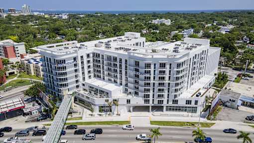 A large white building with a green roof is surrounded by a parking lot.