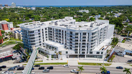 A large white building with a green roof is surrounded by a parking lot.