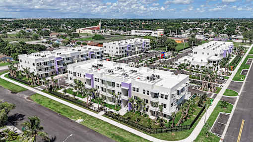 A large white building with a purple stripe on the side is surrounded by a green lawn and a black fence.