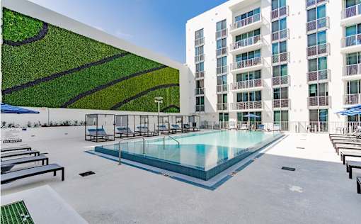 a large pool in front of a building with a green wall