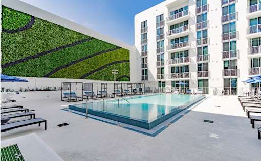 A pool area with a green wall and a white building in the background.