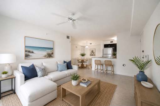 A living room with a white couch, a coffee table, and a painting of a beach scene on the wall.
