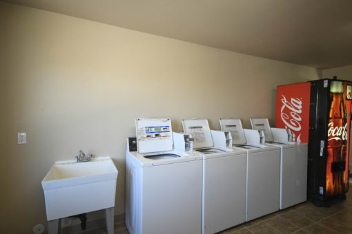 a row of washing machines and a coca cola refrigerator in a laundry room
