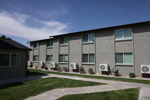 A building with grey walls and multiple air conditioning units in front.